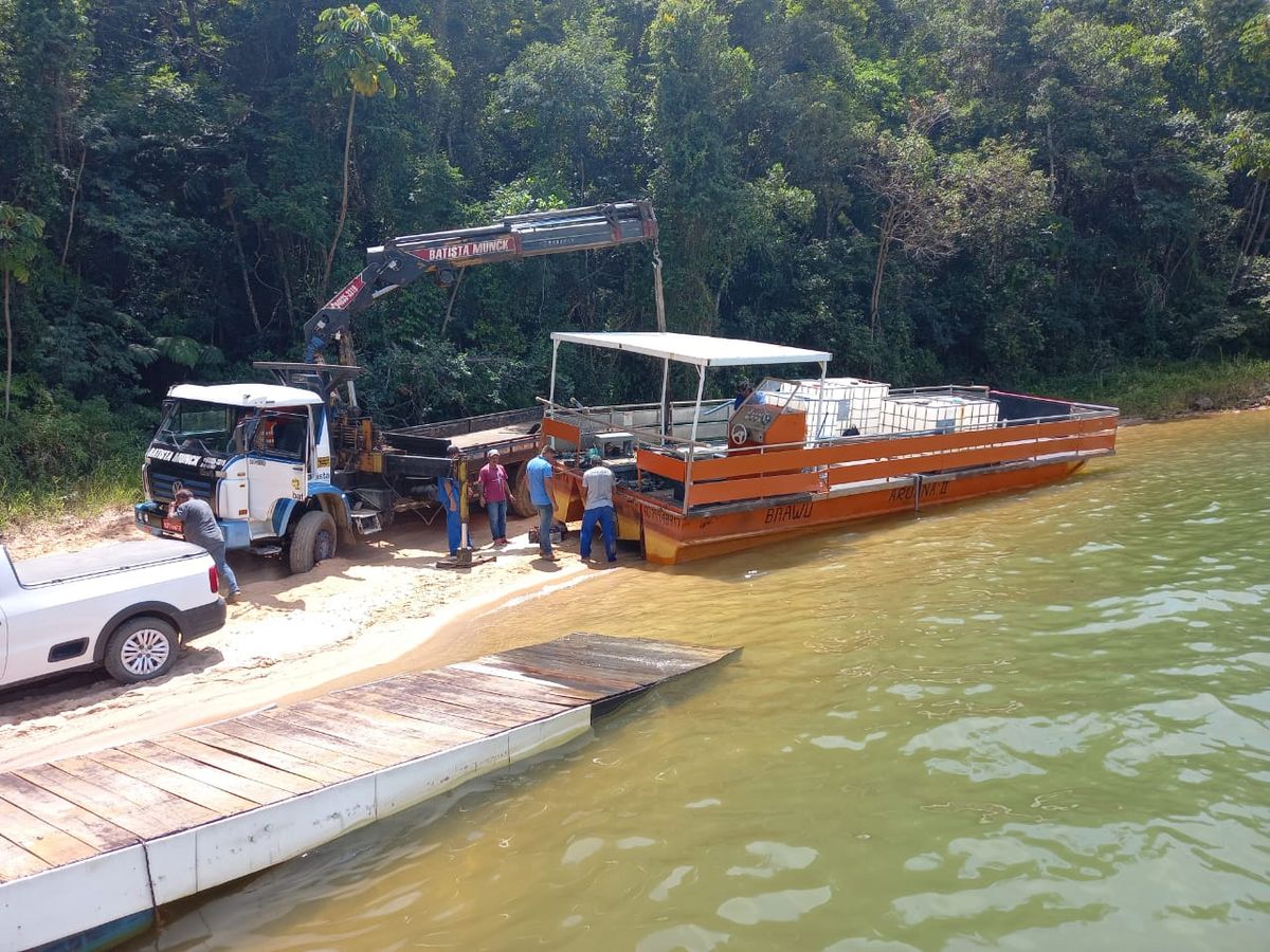 Caminhão munck Batista operando içamento de carga em balsa na beira da represa