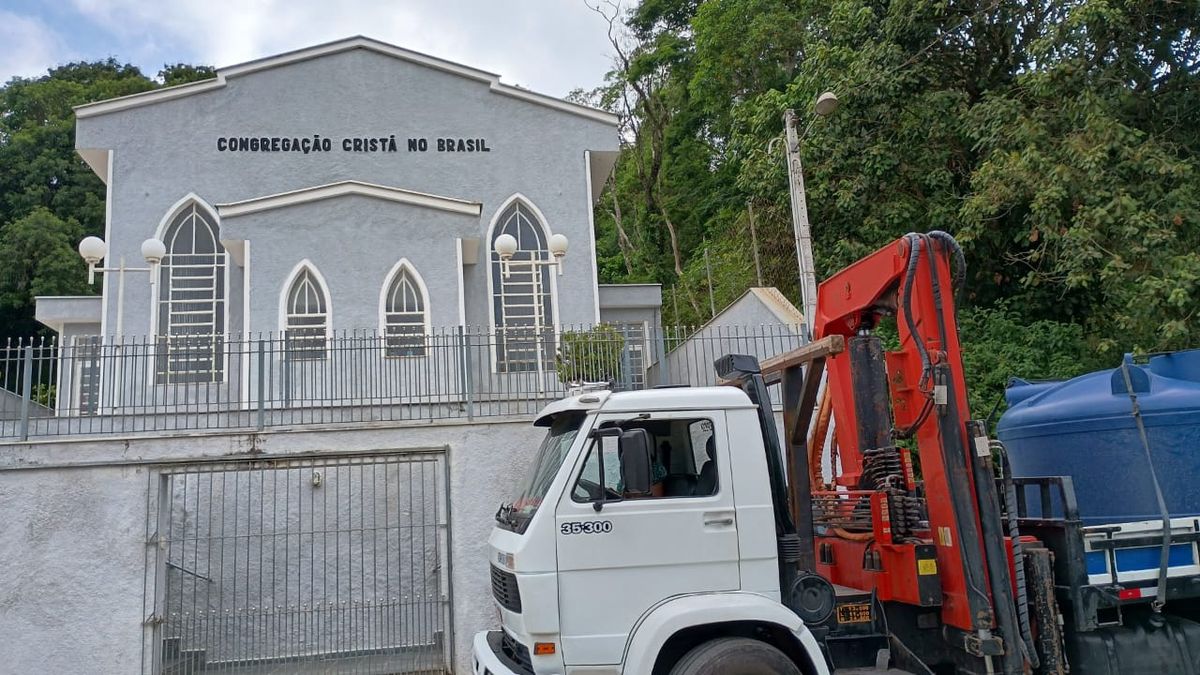 Caminhão munck posicionando caixa d'água em instalação de igreja